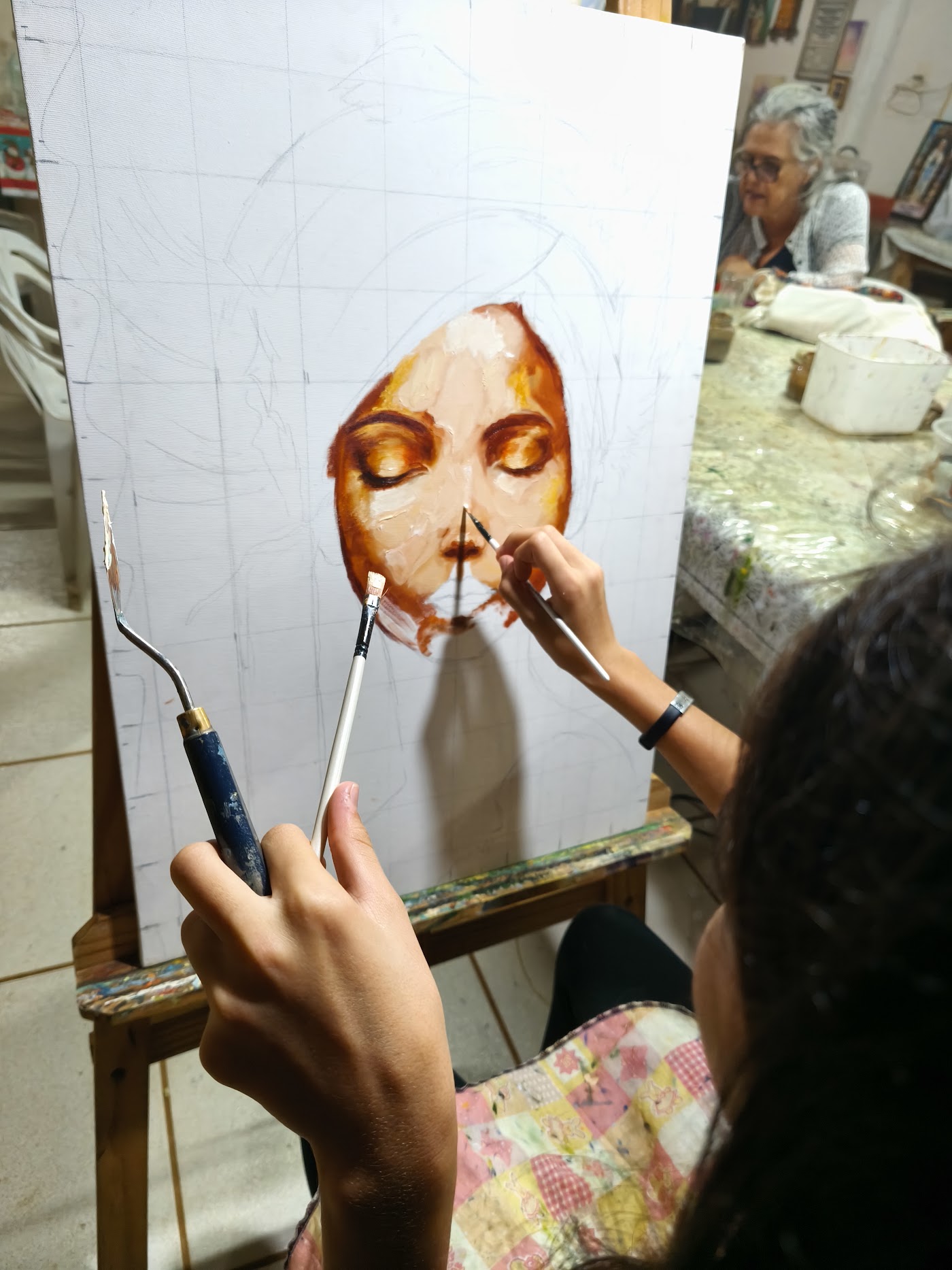 Helena pintando o rosto do retrato com pincel e espátula no cavalete