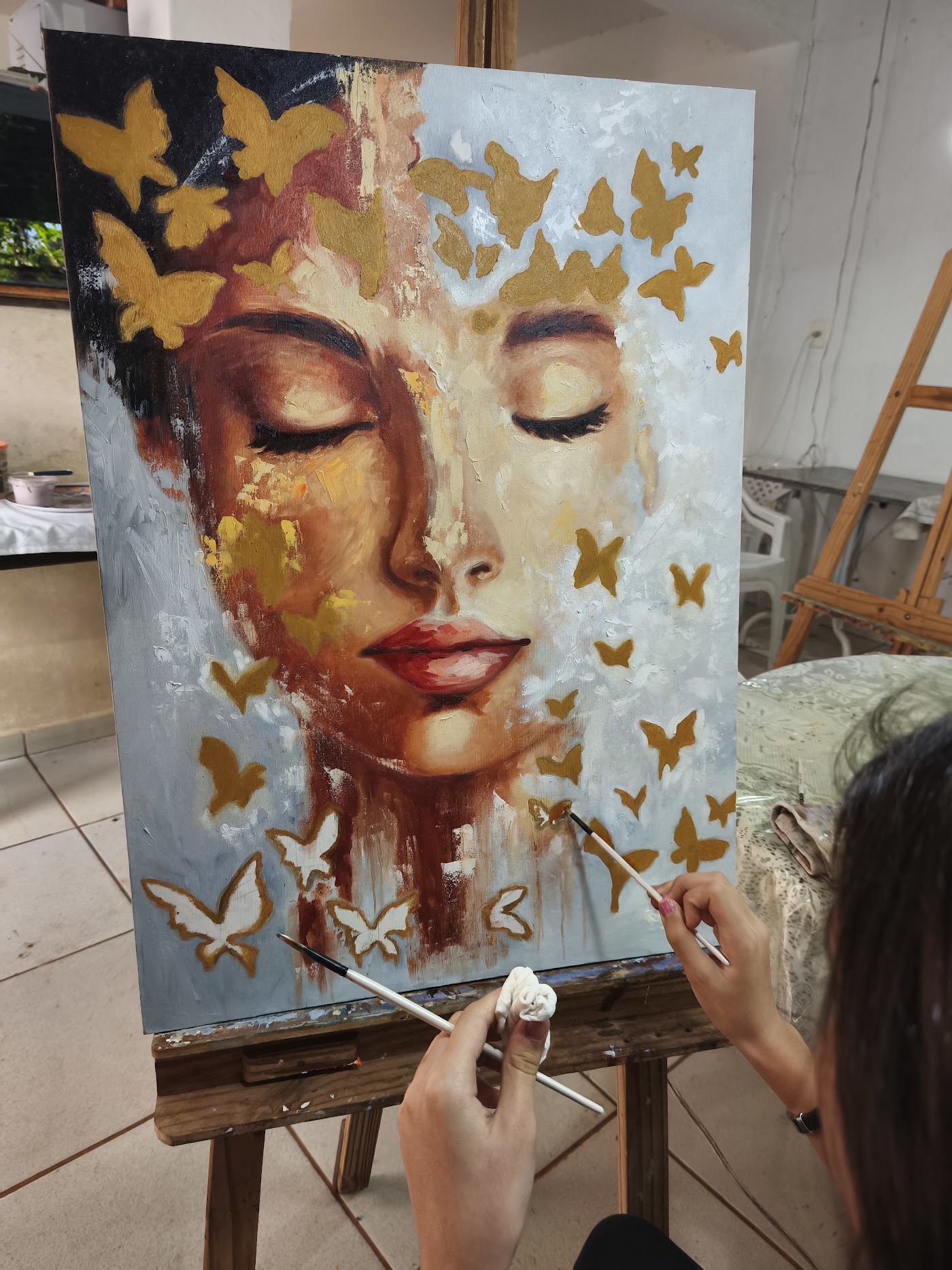 Helena pintando as borboletas em dourado sobre a tela no cavalete